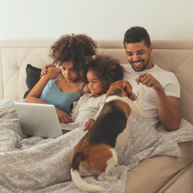 Lifestyle image of a family of three laughing in bed with their dog